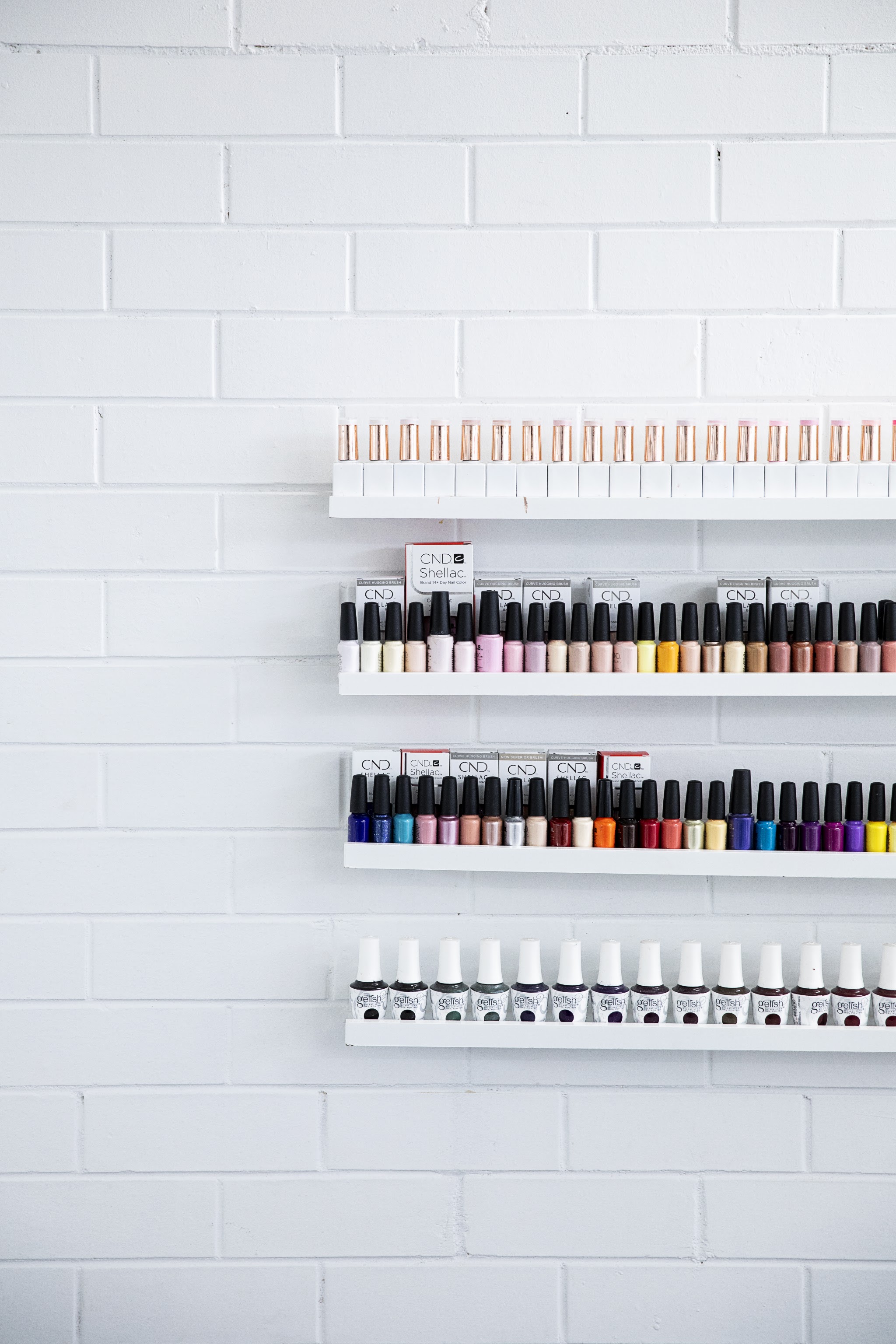 A wall of CND Shellac and Gelish polish colours on white brick